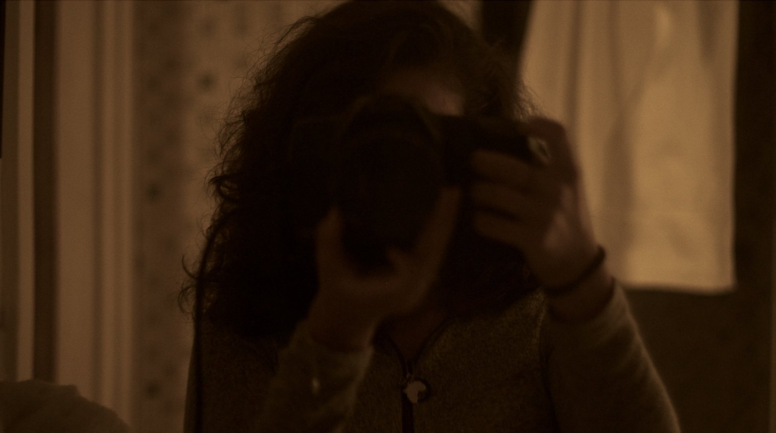 Inès photographing herself in a mirror, in low warm light